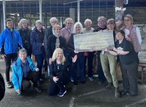 Women gathered around, holding a check symbolizing a generous contribution.